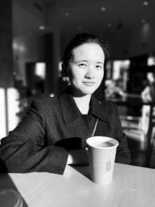 Black and white photo of woman sitting at table with cup of coffee
