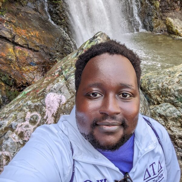 Male smiling at camera standing in front of waterfall